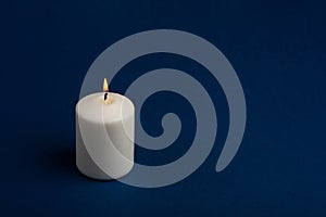 One whiteÃÂ burningÃÂ candle onÃÂ dark blue backgroundÃÂ withÃÂ copyÃÂ space forÃÂ text